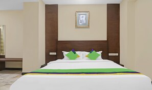 A hotel room with a wooden headboard, a framed picture on the wall, and a bed with a white bedspread and colorful pillows. - SYN Elite Residency (Hyderabad)
