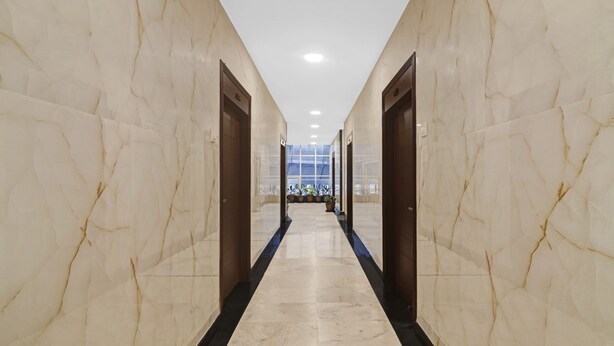 A marble-floored corridor with doors on either side, leading to a room with a large window and potted plants. - SYN Elite Residency (Hyderabad)