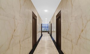 A marble-floored corridor with doors on either side, leading to a room with a large window and potted plants.
