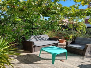 Un espace extérieur aménagé avec des meubles en osier et une table turquoise, entouré d’une végétation luxuriante et sous un ciel dégagé.