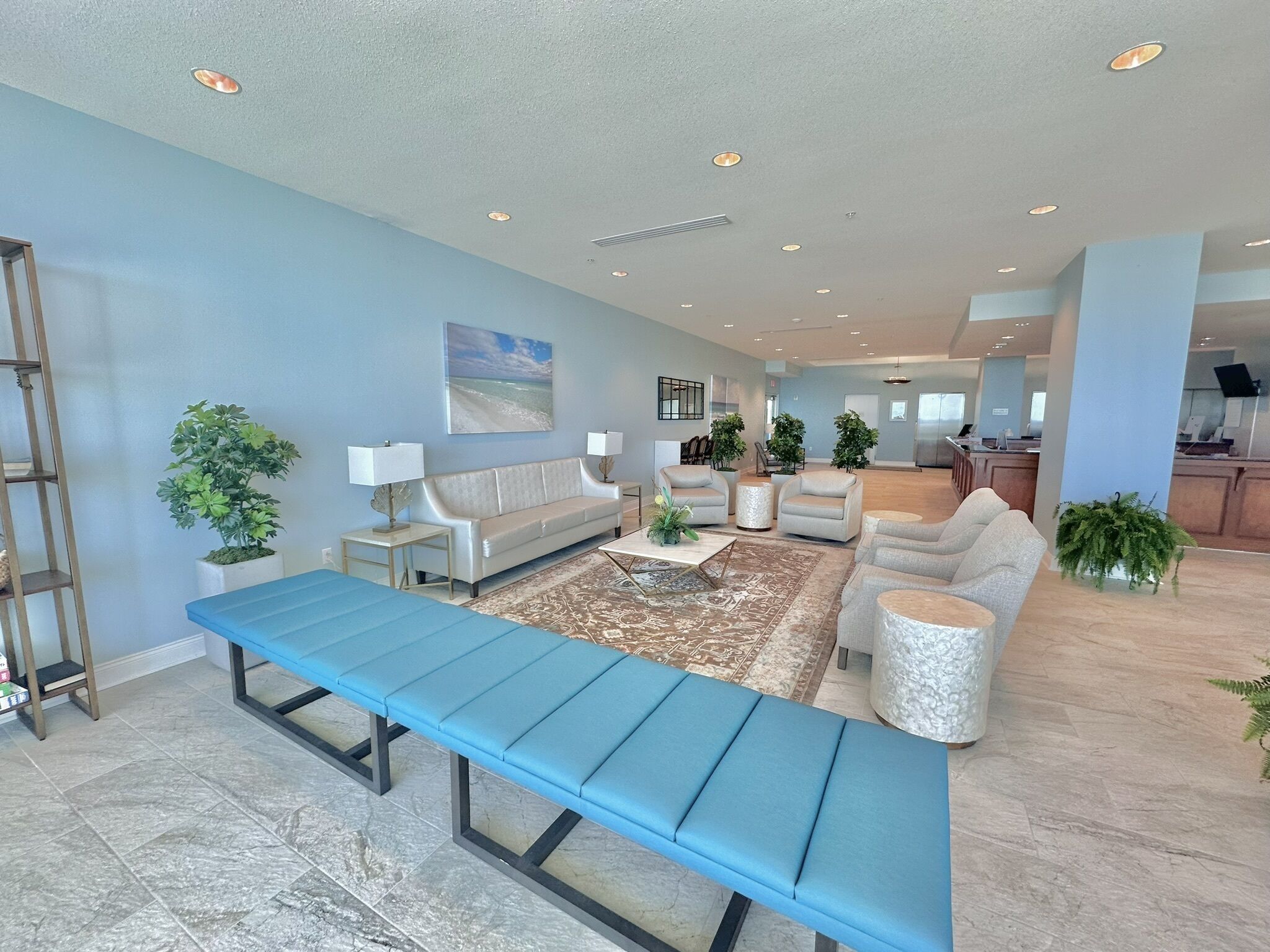A spacious living area with a blue bench, sofas, and potted plants.