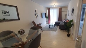 Un salon moderne avec une table à manger en verre, un canapé et un téléviseur fixé au mur.