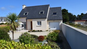 A two-story house with a garage, a patio with outdoor furniture, and a garden with various plants.