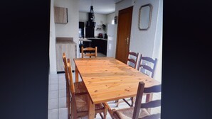 A dining area with a wooden table and chairs, a kitchen in the background, and a door with a mirror.