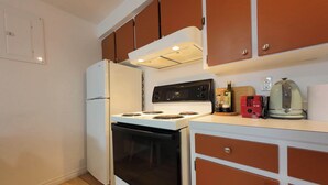 A compact kitchen with a white refrigerator, black oven, and a stove with a digital control panel. - Logis near university, parking & Wi-Fi (Rouyn-Noranda)
