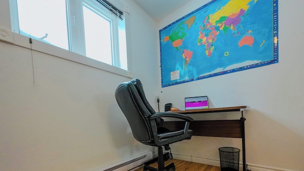 A room with a wooden floor, a black office chair, a desk with a laptop, a world map on the wall, and a window. - Logis near university, parking & Wi-Fi (Rouyn-Noranda)