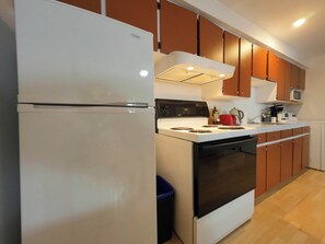 A kitchen with a refrigerator, stove, microwave, and wooden cabinets. - Logis near university, parking & Wi-Fi (Rouyn-Noranda)
