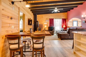 Un accogliente interno di una baita con un'area pranzo in legno, un caminetto, un soggiorno con divano e TV, e una parete di accentazione rossa.