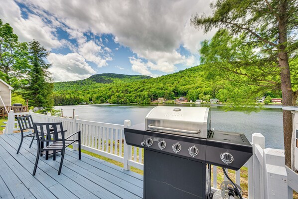 Una terrazza con barbecue e sedie che si affaccia su un lago e colline boscose.