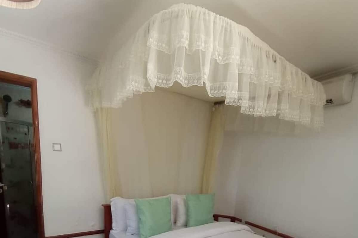 A single-bed room with a wooden frame, white bedding, and a green accent pillow.