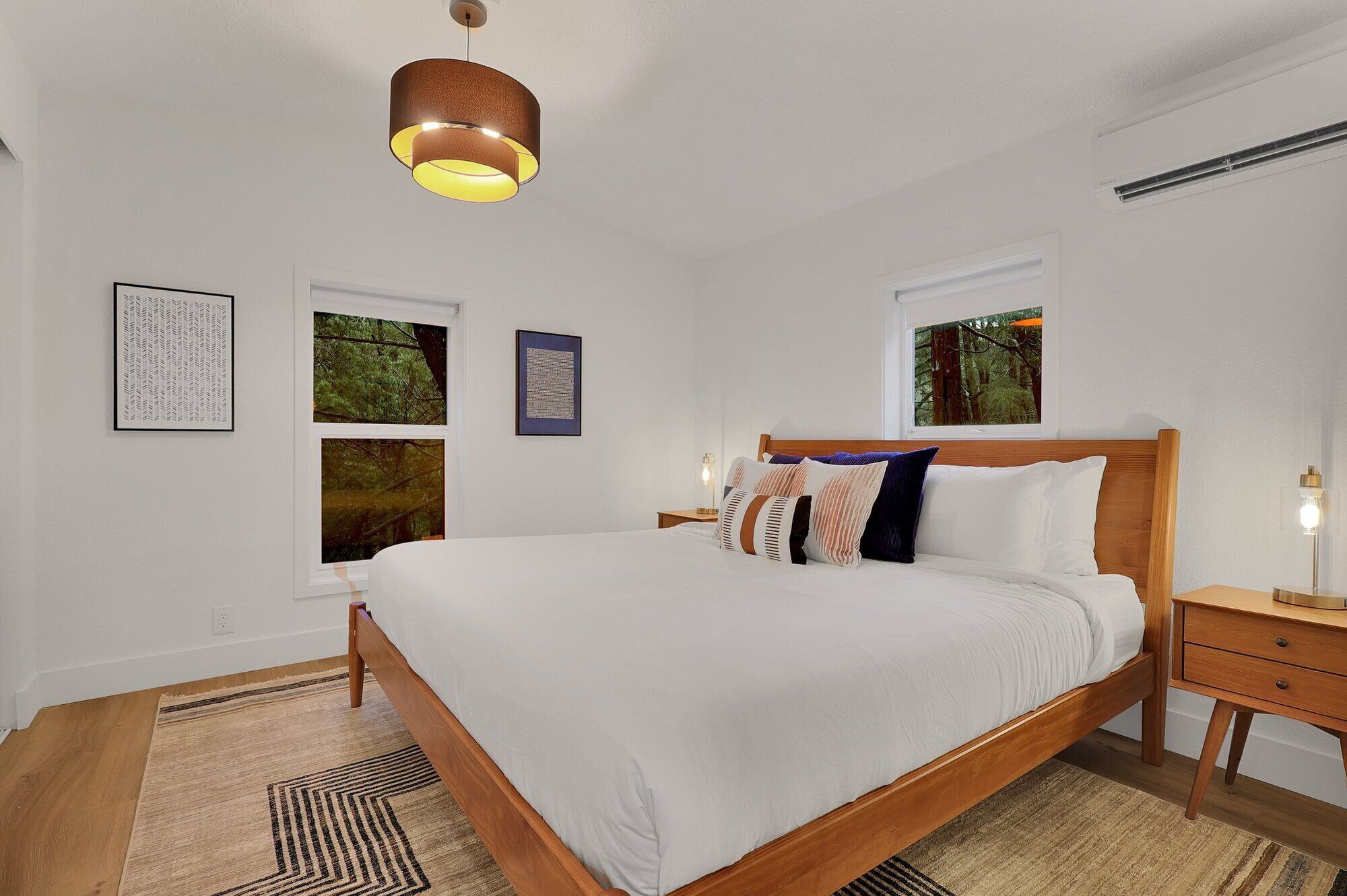 Um quarto com cama de madeira, mesa de cabeceira, abajur e quadros na parede.