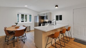 Uma cozinha moderna com armários brancos, uma ilha central e banquetas.
