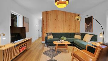 Uma sala de estar moderna com uma parede de destaque em madeira, um sofá verde, uma mesa de centro de madeira e uma TV em um suporte de madeira.