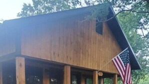 A wooden cabin with a porch, an American flag, and a small garden area.