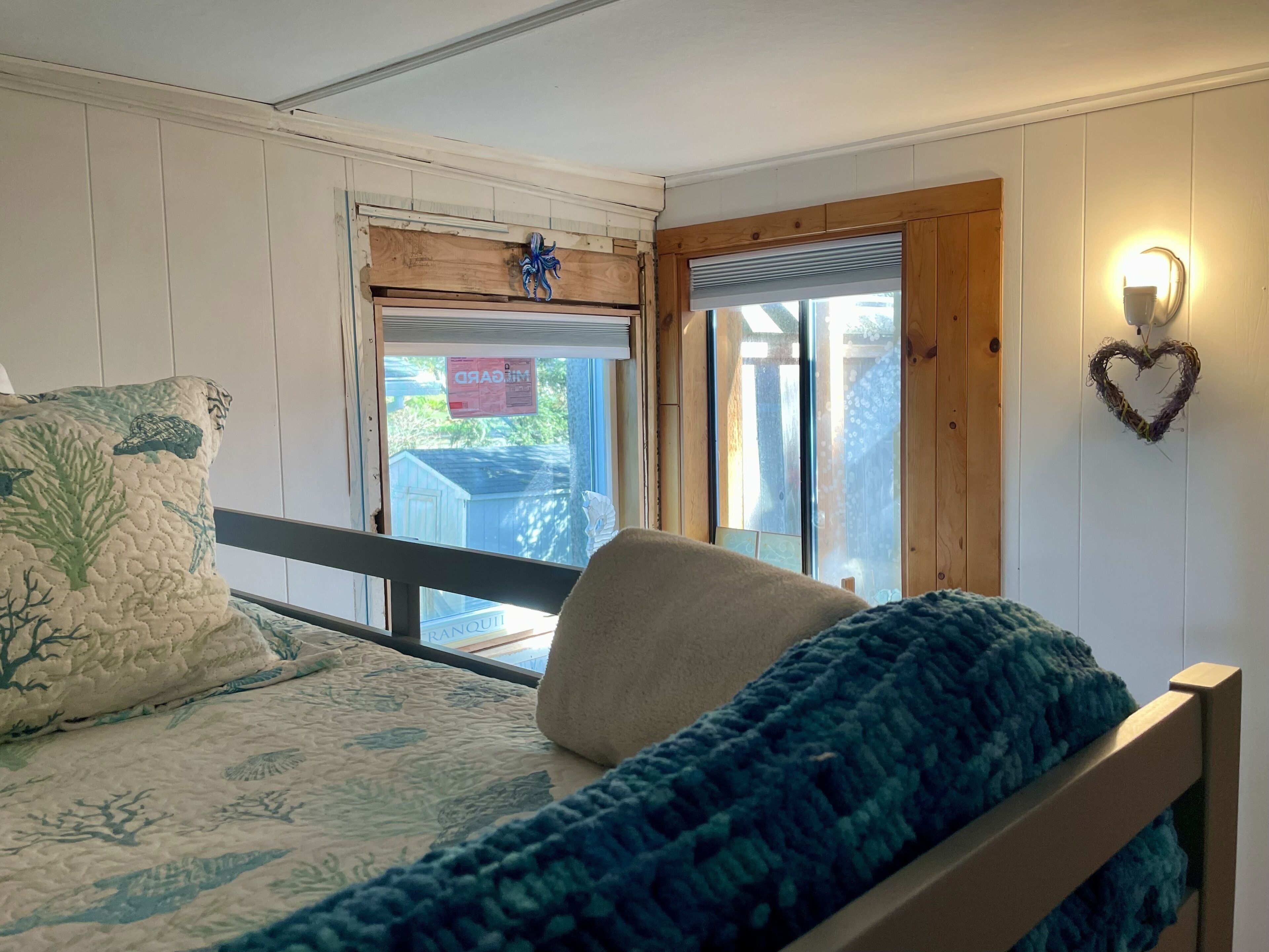 A bedroom with a bed, a window, and a heart-shaped wall decoration.