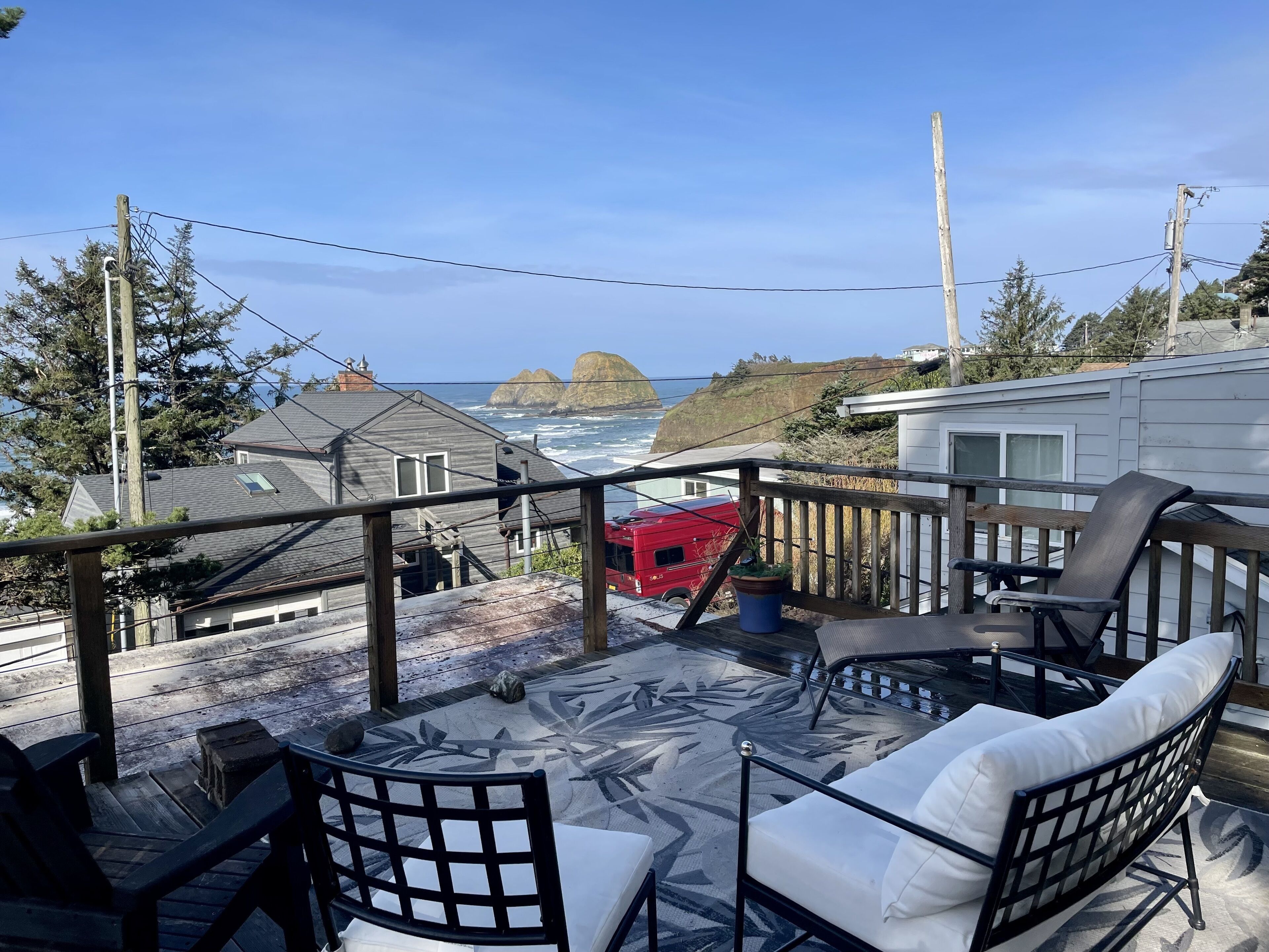 A deck with outdoor furniture, a view of the ocean, and houses in the background.