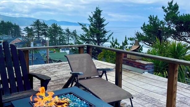 Een terras met een vuurplaats, lounge fauteuils en uitzicht op bergen en bomen.