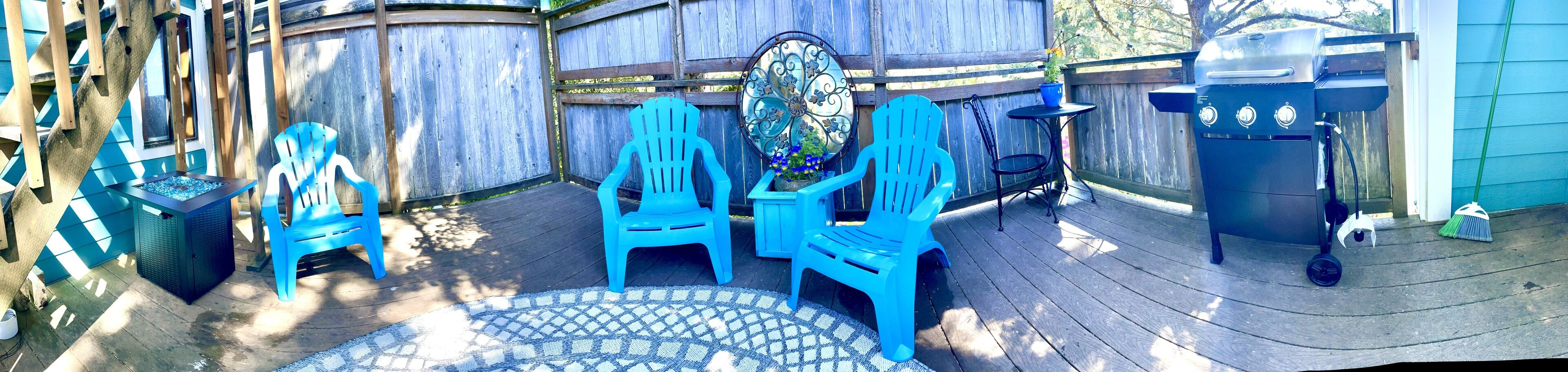 A wooden deck with blue plastic chairs, a metal grill, and a decorative mirror.