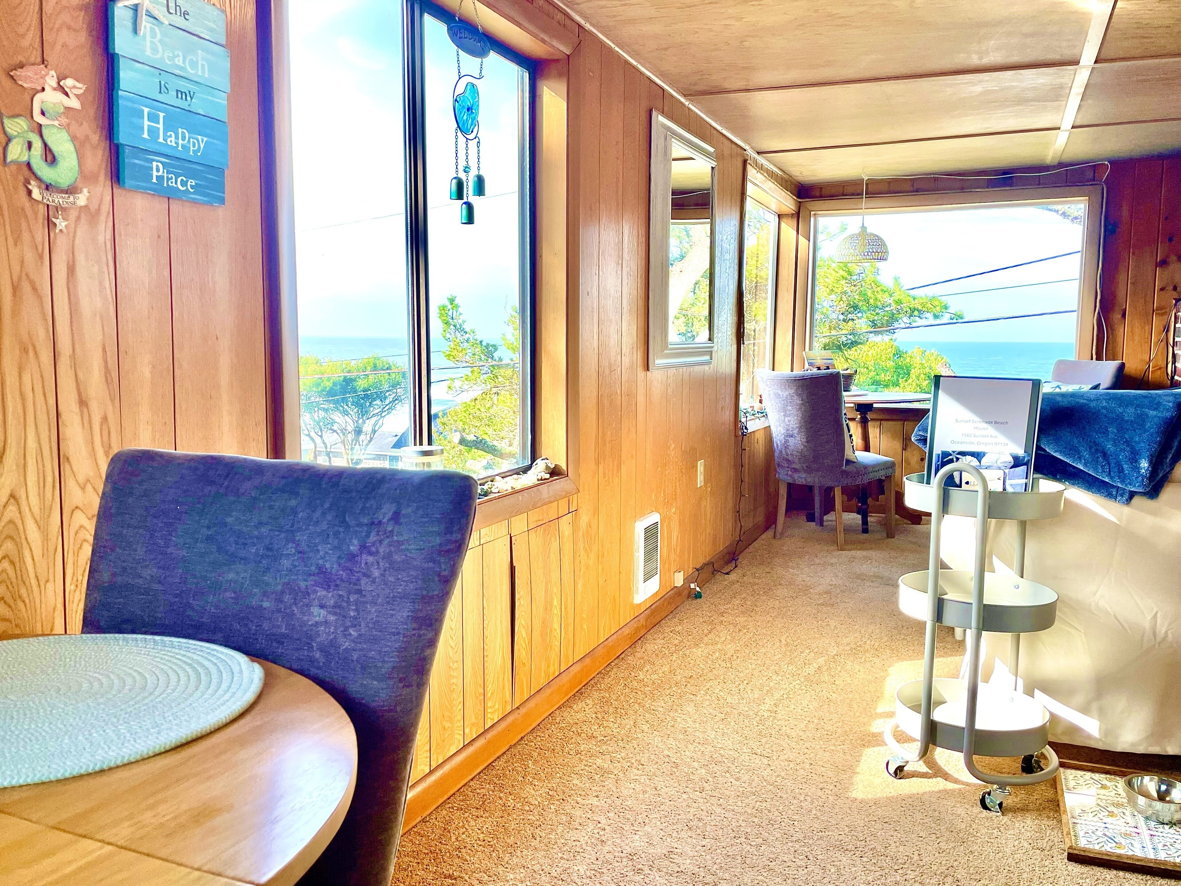 Une chambre avec vue sur la plage, des murs en bois, une table ronde, une chaise et un lit avec un oreiller bleu.