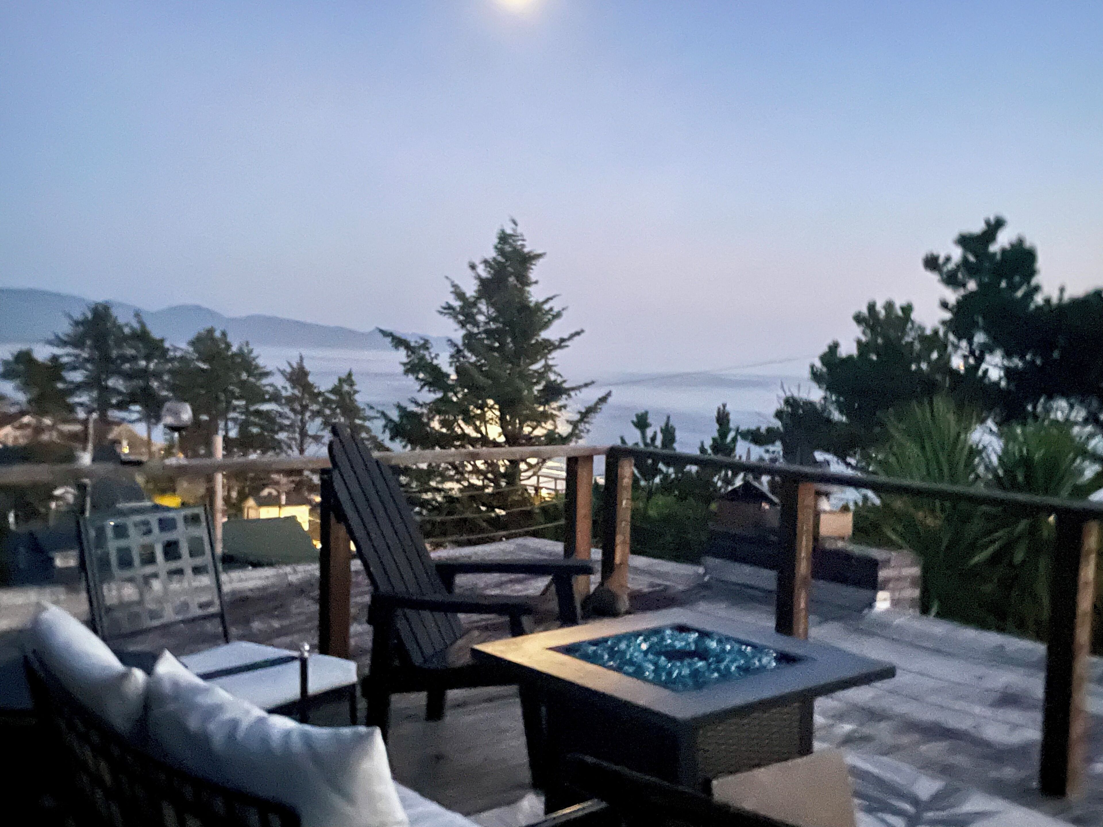 A terrace with outdoor seating, a fire pit, and a view of the sea and mountains.