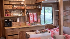 Een gezellig blokhut interieur met houten wanden, een kitchenette, een eethoek en een raam met uitzicht op groen.