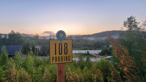 A parking sign with a location marker, surrounded by trees and a view of a body of water and hills in the background. - EXPLORE Munising Studio Suite 112 (Munising)