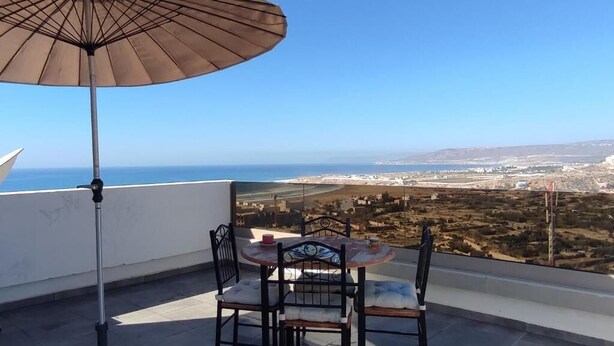 Une terrasse avec une table et des chaises, un parasol et une vue sur la côte.