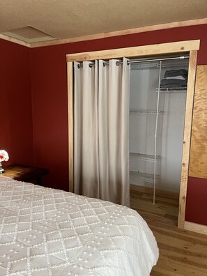 A bedroom with a bed, a wooden floor, a red wall, a sliding door closet, and a nightstand with a lamp.