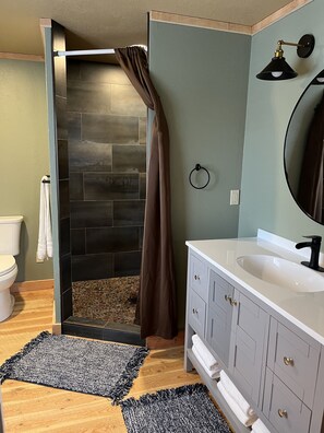 A bathroom with a shower, a toilet, a sink, and a mirror.