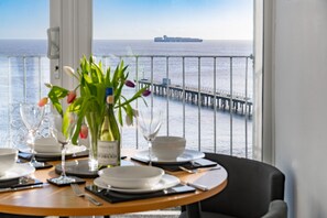 Ein Esstisch ist gedeckt mit Tellern, Gläsern und einer Blumenvase, mit Blick auf einen Steg und das Meer.