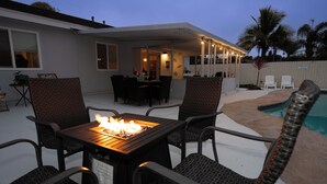 An outdoor patio with a table and chairs, a fire pit, and a pool area.