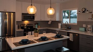 A modern kitchen with stainless steel appliances, a central island with seating, pendant lighting, and a view of the outdoors.