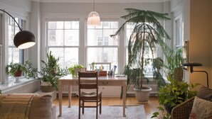 Una habitación acogedora con un escritorio de madera, una silla, un sofá y varias plantas en macetas.