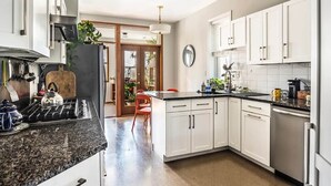 Una cocina moderna con armarios blancos, encimera de granito y refrigerador de acero inoxidable.