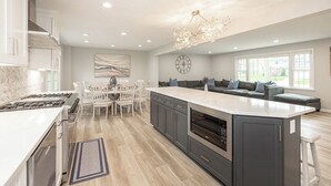 Een moderne keuken met een centraal eiland, witte kastjes en een eethoek met witte stoelen.
