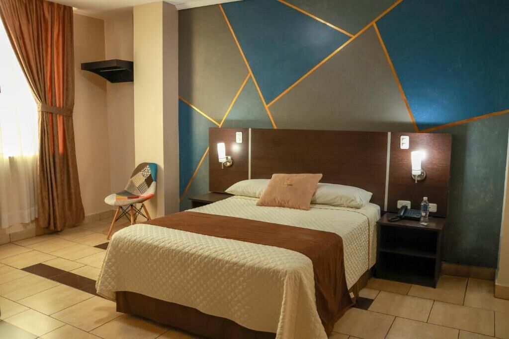 A hotel room with a large bed, a nightstand, a chair, and a wall with geometric patterns.