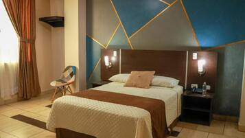 A hotel room with a large bed, a nightstand, a chair, and a wall with geometric patterns.
