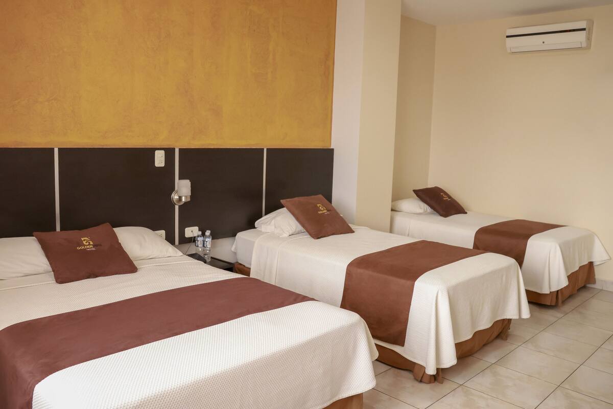 A hotel room with three beds, each with a brown headboard and white bedding.