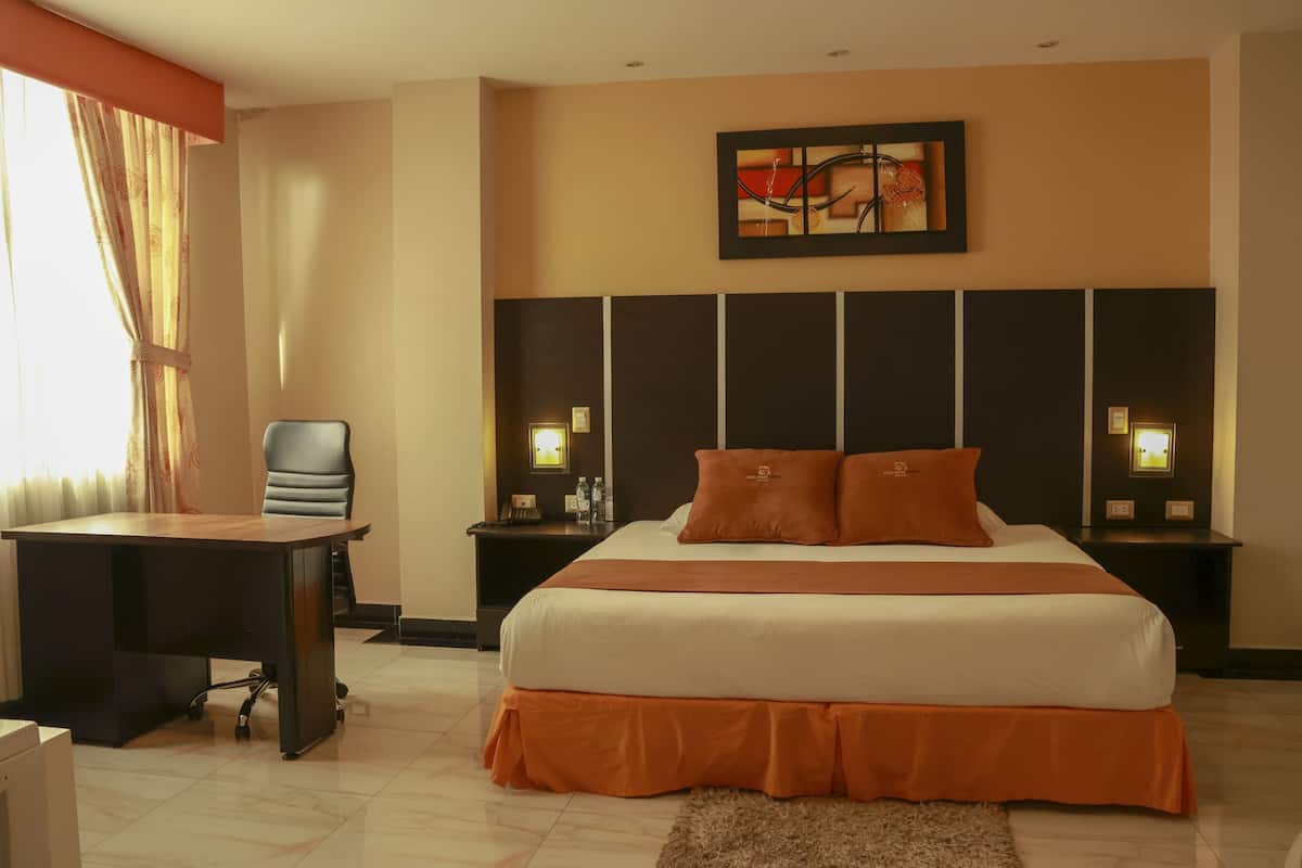 A hotel room with a large bed, a desk, and a chair. There are two bedside tables with lamps.
