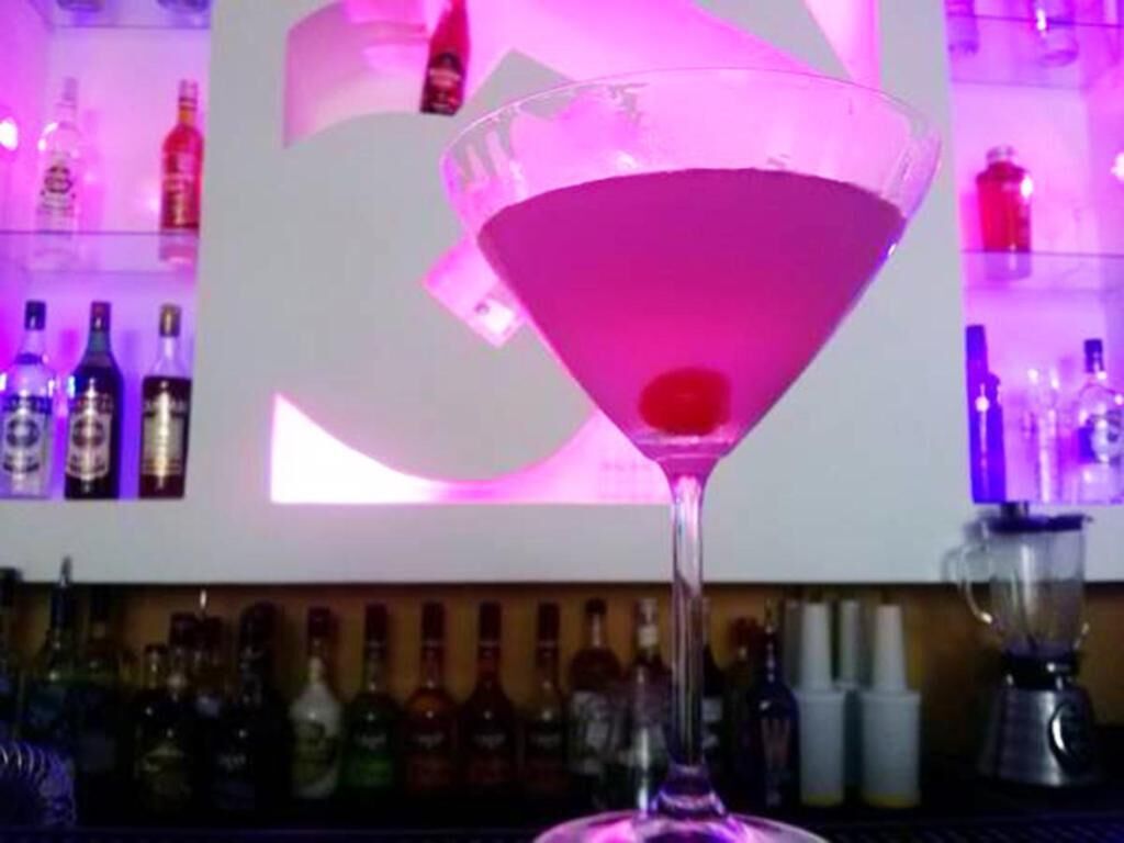 A martini glass with a pink liquid on a bar counter.