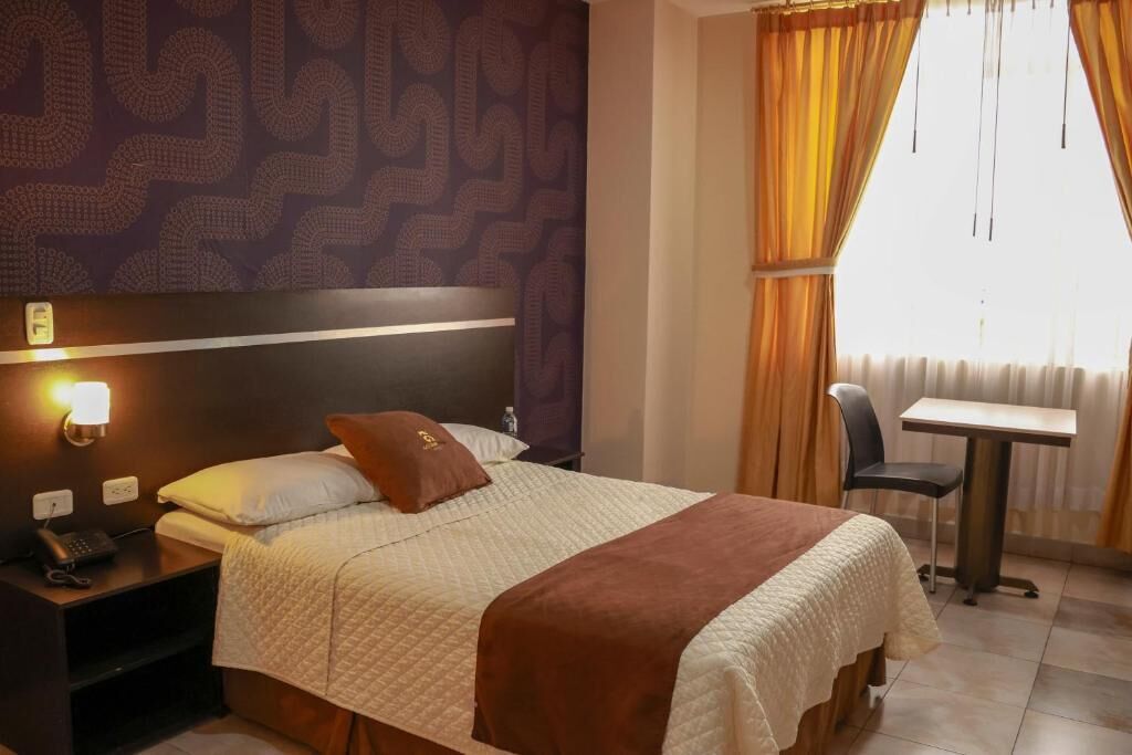 Een hotelkamer met een bed, een nachtkastje met een telefoon, een tafel en een stoel.