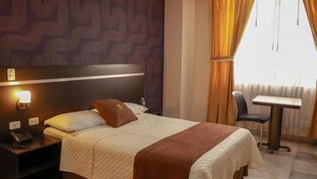 Een hotelkamer met een bed, een nachtkastje met een telefoon, een tafel en een stoel.