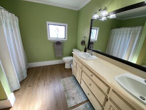 A bathroom with green walls, a white toilet, a beige vanity with a large mirror, and a window above the toilet.