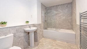 A modern bathroom with a bathtub, a pedestal sink, and a shower. - Gospel Heights by Guestz (Heswall)
