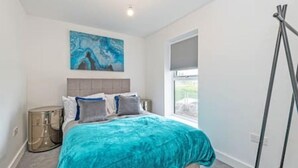 A bedroom with a bed, a painting, a window, and a floor lamp. - Gospel Heights by Guestz (Heswall)