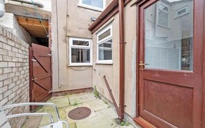 Outdoor space with a red door and window, featuring a metal chair and concrete paving.