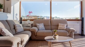 A modern living room with a beige sofa set, a round coffee table, and a view of a coastal town through large windows. - Kladissos Family Seaside Villa with heated pool, hydromassage and barbecue! (Agia Pelagia)