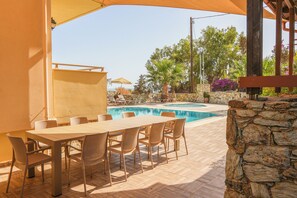 An outdoor pool area with a table and chairs, surrounded by stone walls and greenery. - Kladissos Family Seaside Villa with heated pool, hydromassage and barbecue! (Agia Pelagia)