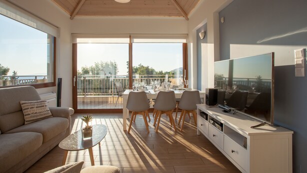 A modern living room with a sofa, coffee table, TV, and dining area with chairs and a table. - Kladissos Family Seaside Villa with heated pool, hydromassage and barbecue! (Agia Pelagia)