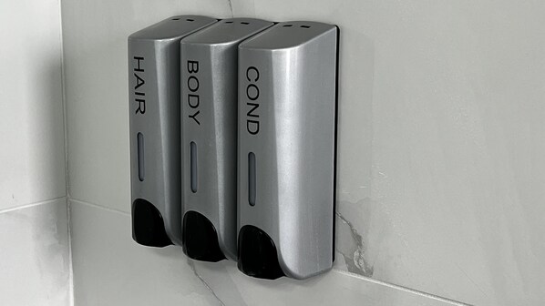 A wall-mounted dispenser with labels for hair, body, and hand sanitizer.